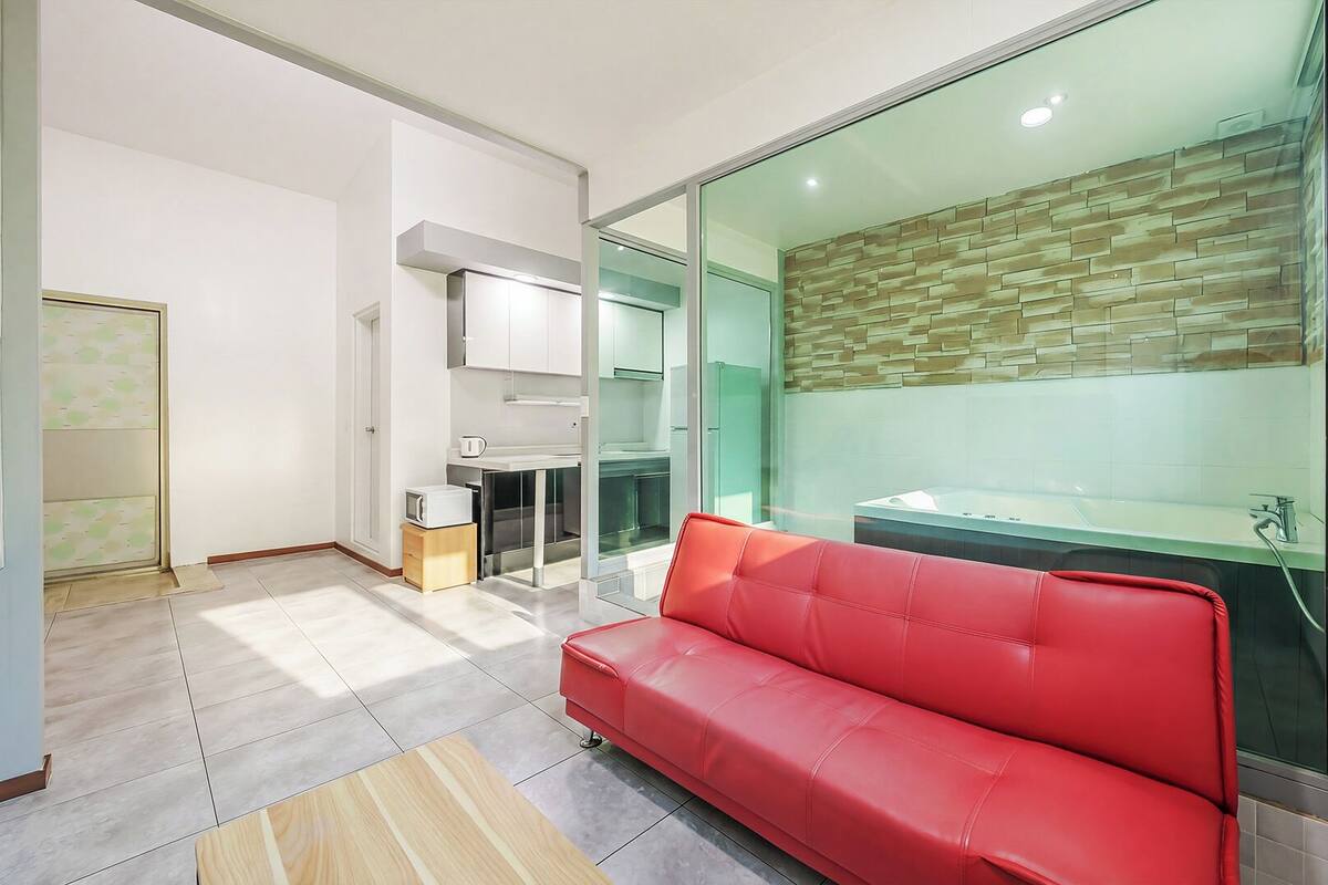 A modern kitchen with a glass partition, a red leather sofa, and a bathroom with a tiled wall.