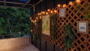 A balcony with a wooden lattice wall, framed botanical prints, and hanging lanterns.