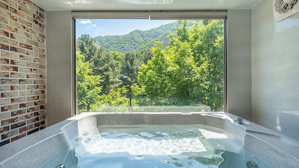 Une salle de bain avec une baignoire, une grande fenêtre et un mur en briques.