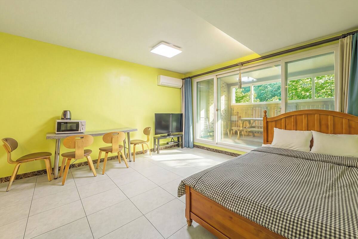 A hotel room with a bed, a desk with a TV, chairs, and a balcony with a view.