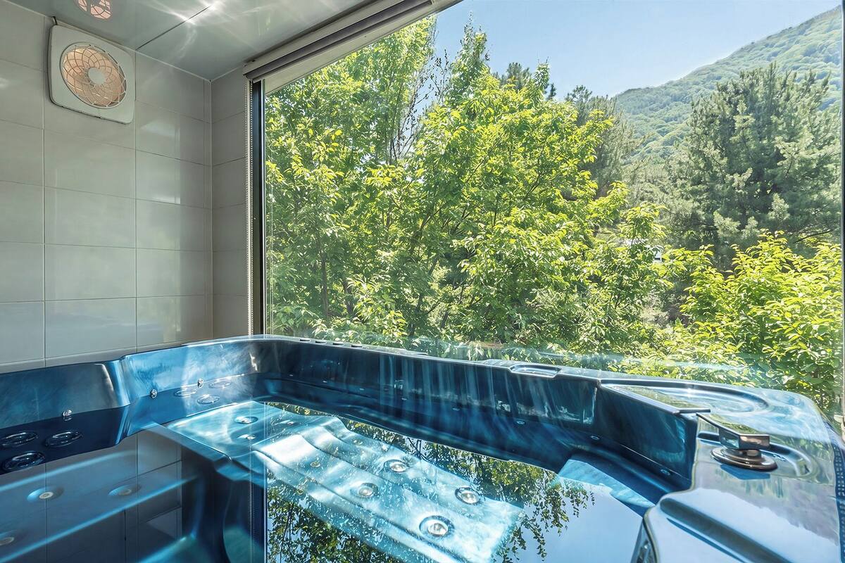 A spa room with a large window, a bathtub, and a shower area.