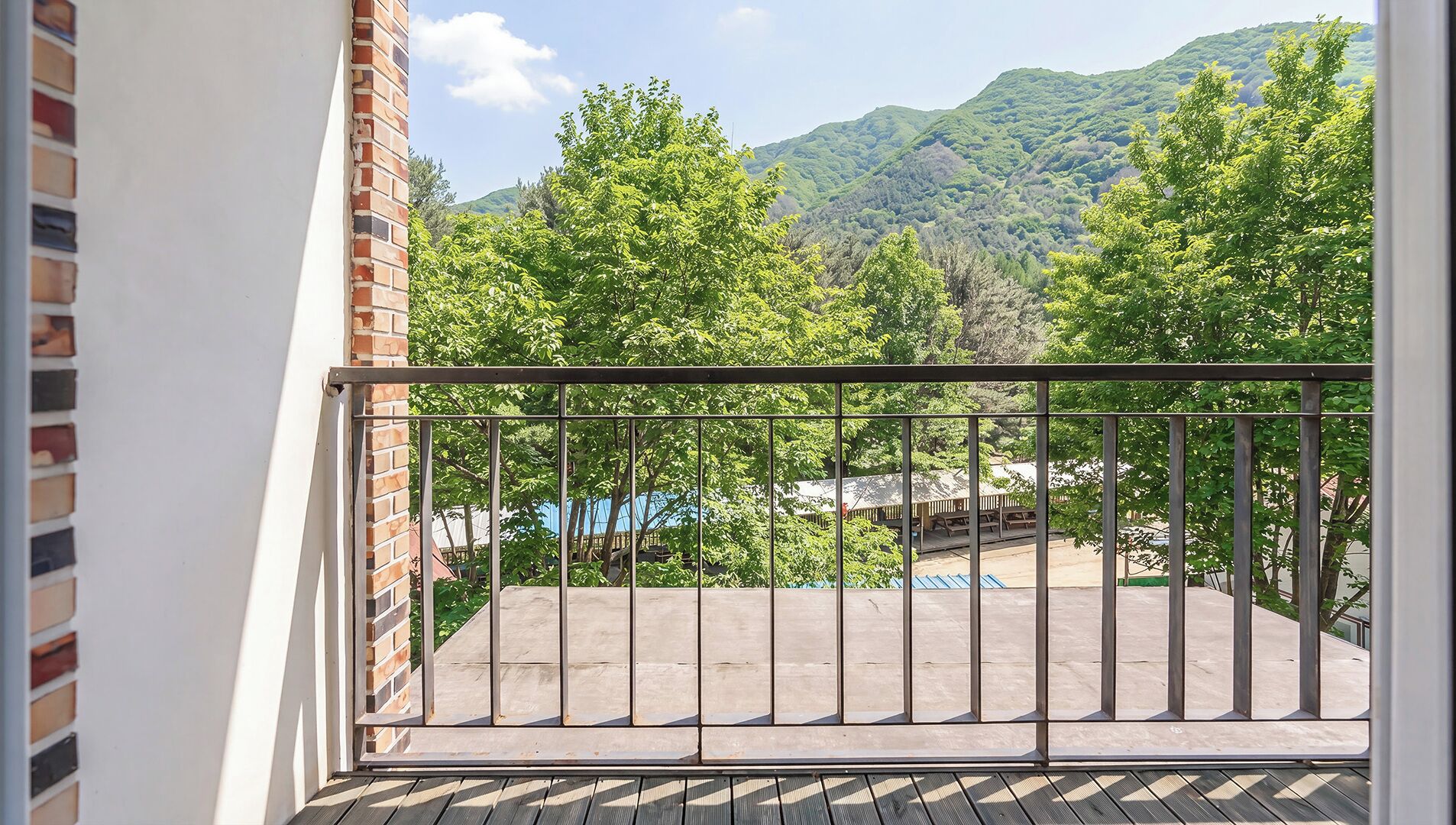 A balcony with a metal railing, a brick wall, and a view of a forested mountain range.