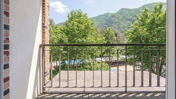 A balcony with a metal railing, a brick wall, and a view of a forested mountain range.