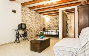 A room with a stone wall, wooden beams, a bed, a small table with a television, and a bathroom visible through an open door. - Vacation home Antonio in the old town of Vrbnik, beautifully furnished (Vrbnik)
