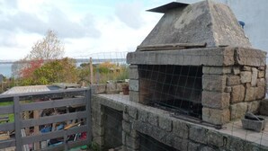 A stone-built outdoor structure with a wire mesh enclosure, possibly a barbecue area, adjacent to a white wall and a fenced garden area. - Family home on the Breton Crozon Peninsula, dogs welcome, view on the sea (Lanvéoc)