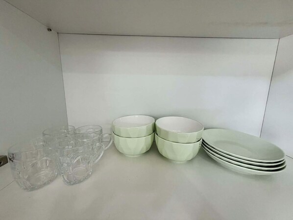 A kitchen with white cabinets, clear glassware, and light green ceramic dishes.