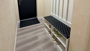 Ein Flur mit einer schwarzen Tür, einem Schuhregal mit mehreren Schuhpaaren und einer hellen Wand.