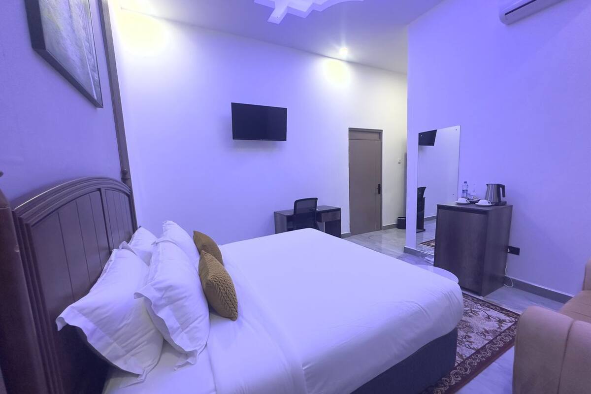 A bedroom with a bed, a desk, a chair, a television, and a mirror.