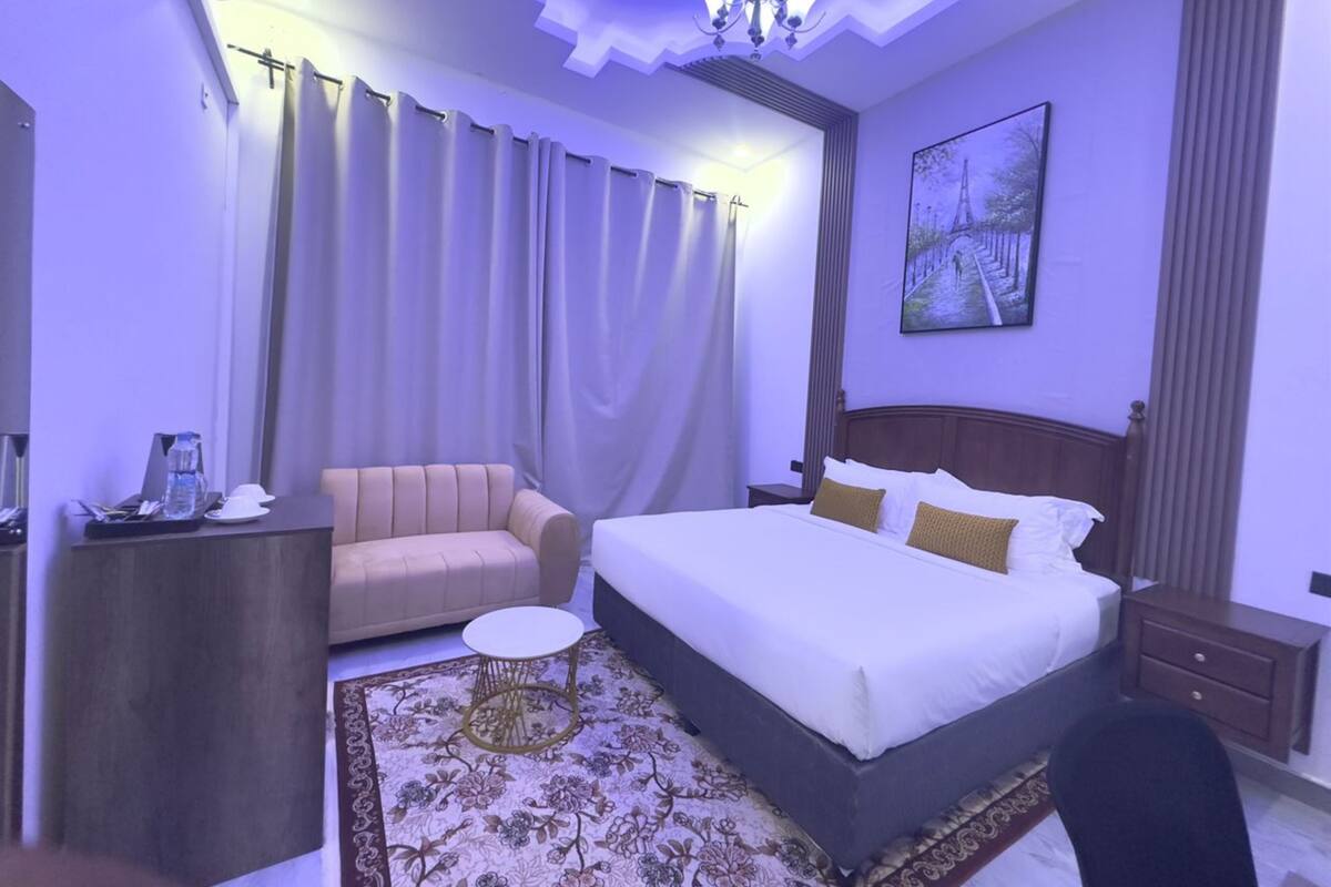 A hotel room with a bed, a sofa, a small round table, a desk, and a nightstand.