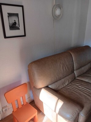 Ein braunes Ledersofa, ein kleiner orangefarbener Sessel und ein gerahmtes Bild an der Wand.