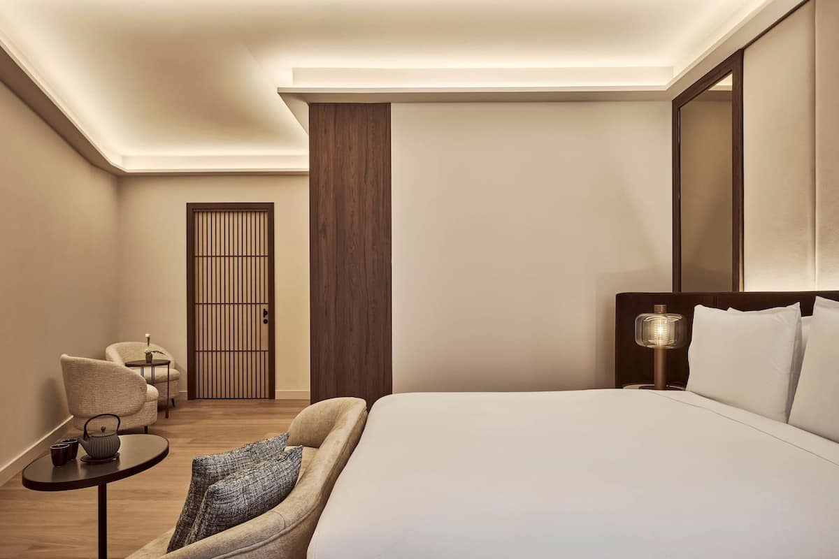 Une chambre d’hôtel avec un lit, un canapé, une petite table avec une lampe et une vue sur une porte en bois.