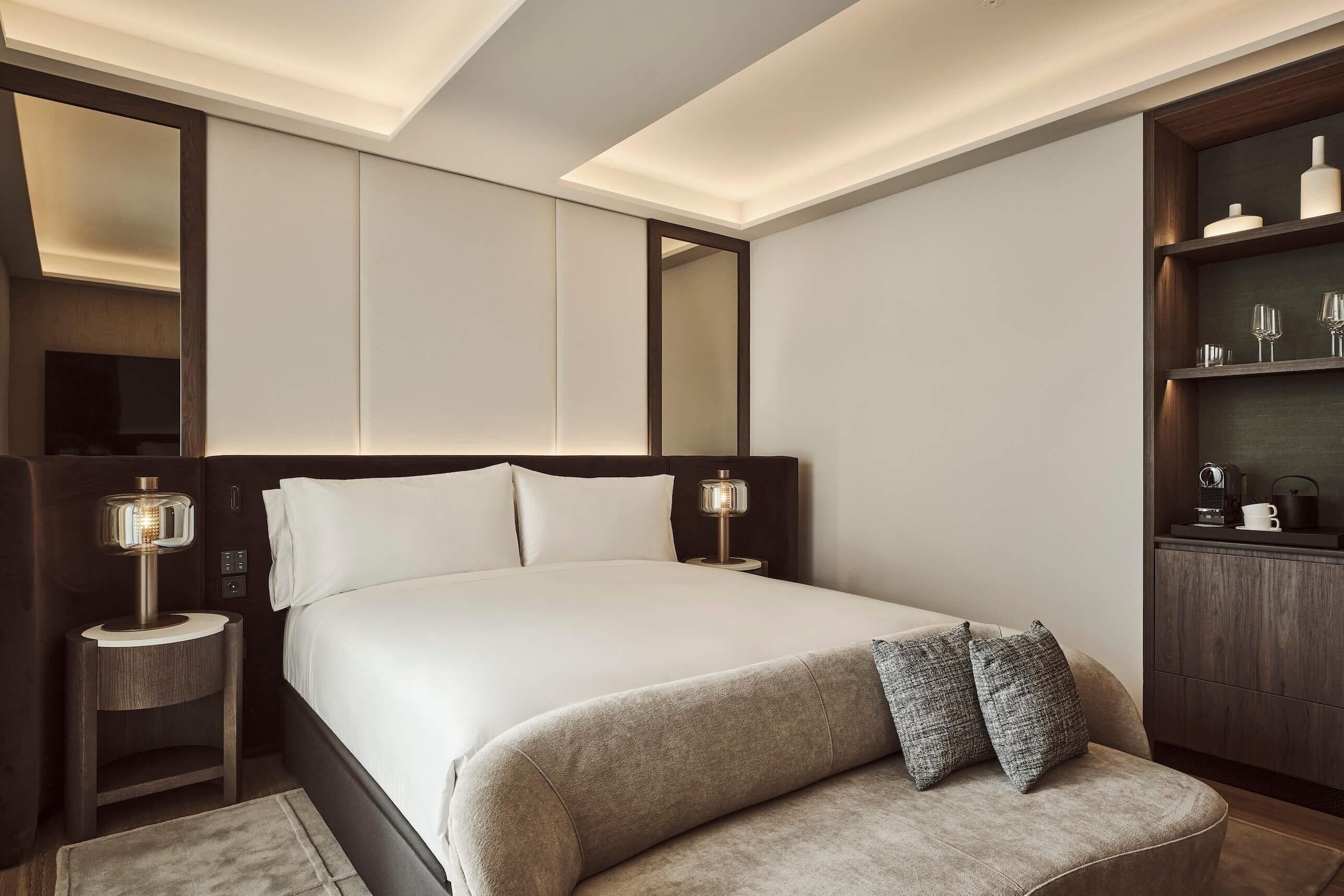 A modern hotel room with a large bed, bedside lamps, a built-in wardrobe, and a bedside table.