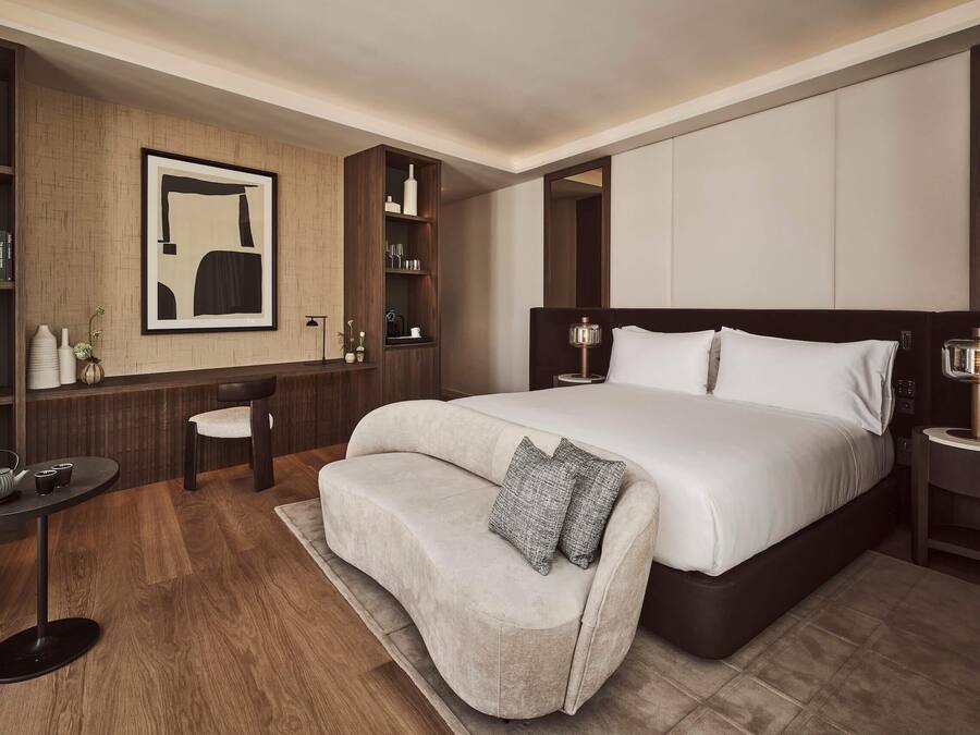 Una habitación de hotel moderna con una cama grande, un sofá, una mesita con un hervidor de agua y una estantería.