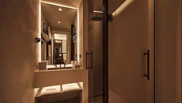 A modern bathroom with a glass shower enclosure, a built-in sink with a mirror, and a bench with towels.