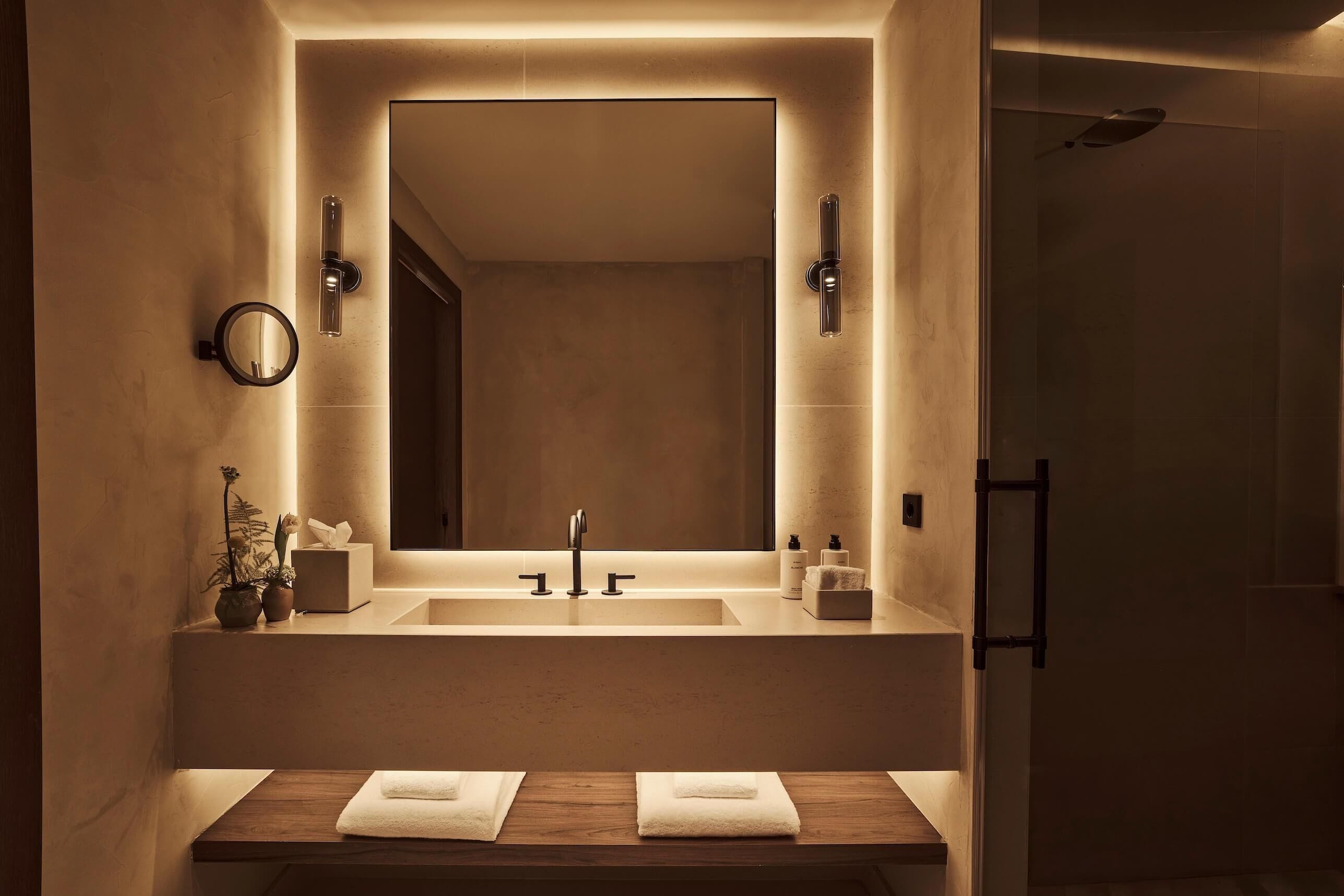 A modern bathroom with a large mirror, two sinks, and a shower area.