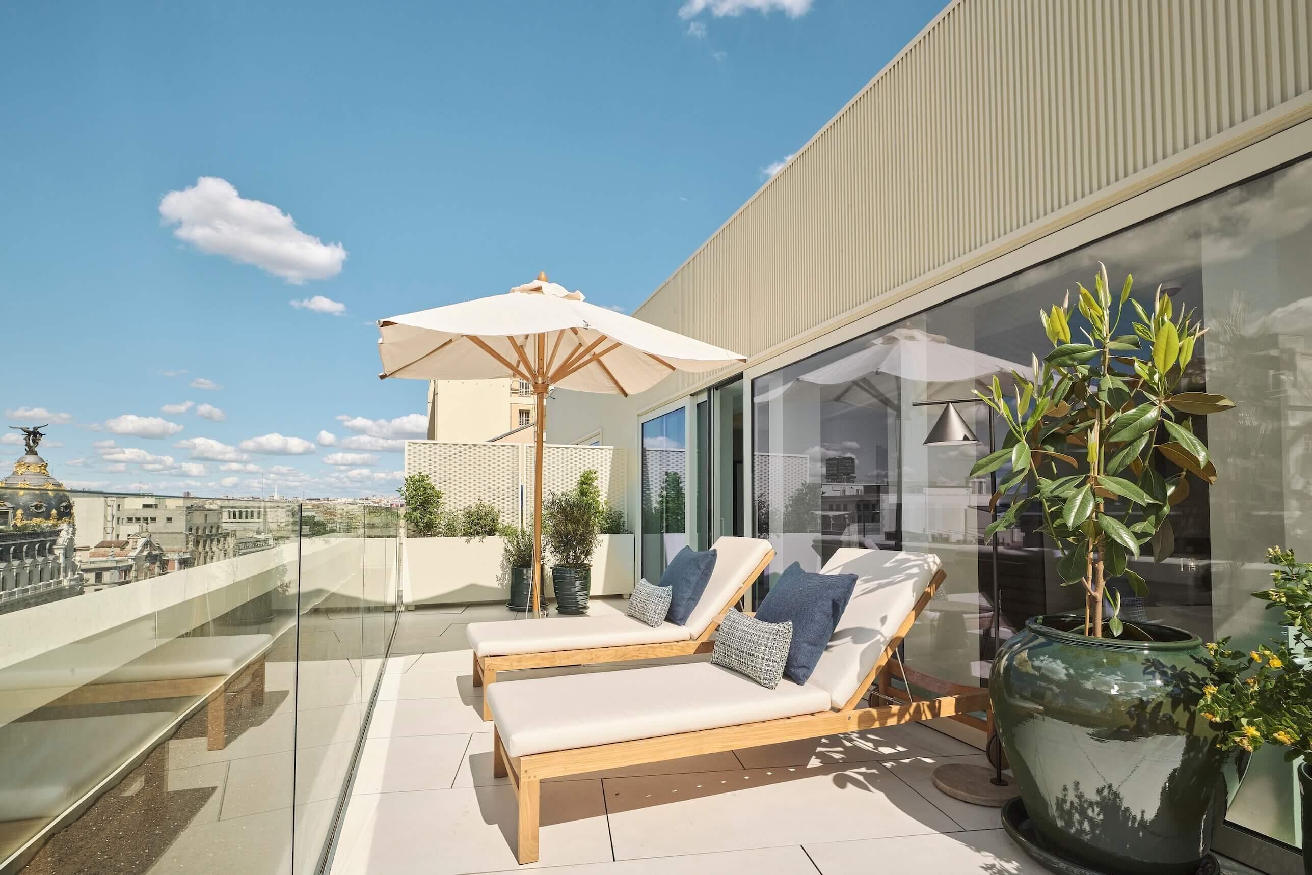 A rooftop terrace with lounge chairs, a large umbrella, and potted plants.