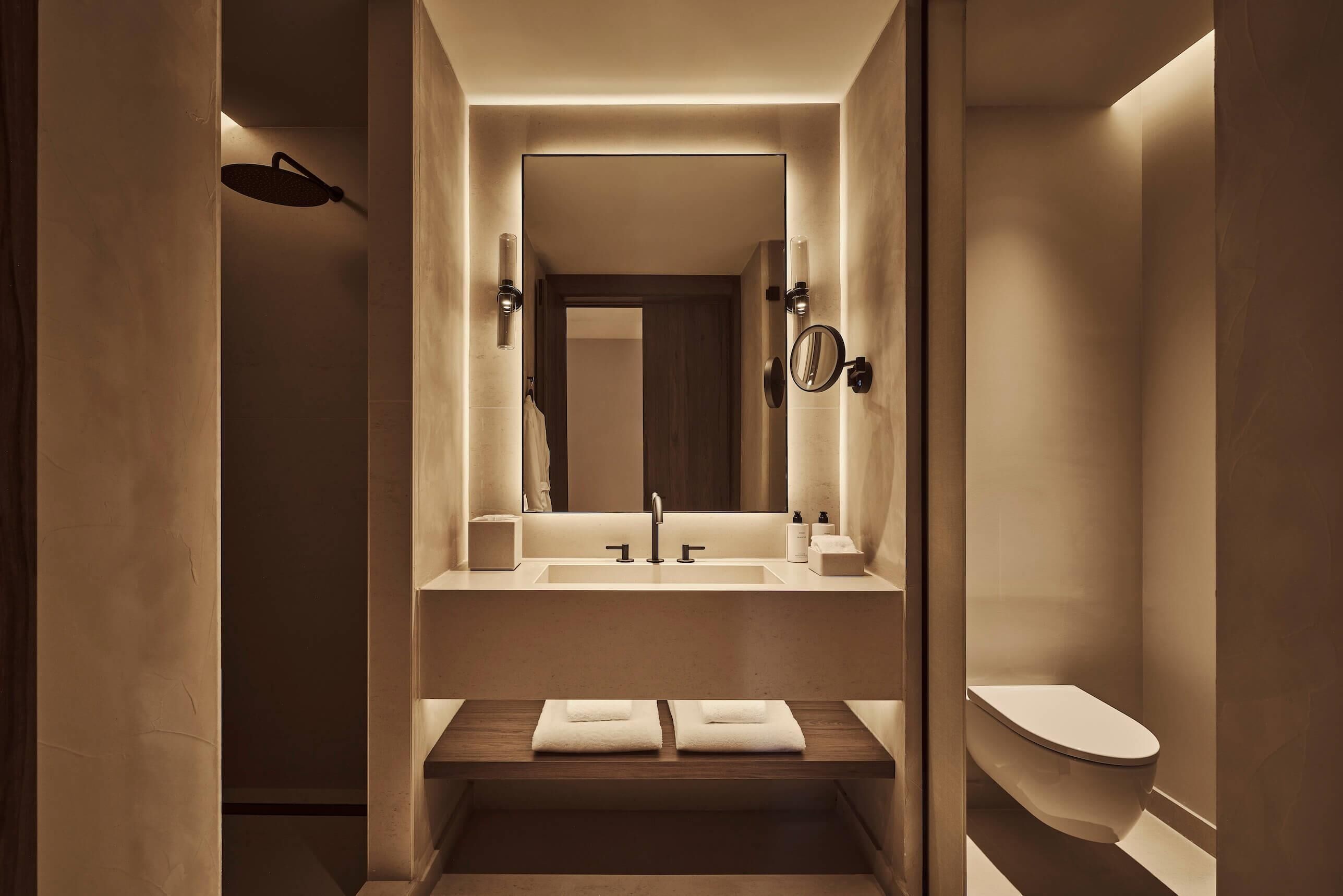 A modern bathroom with a large mirror, a sink, a toilet, and a towel rack.