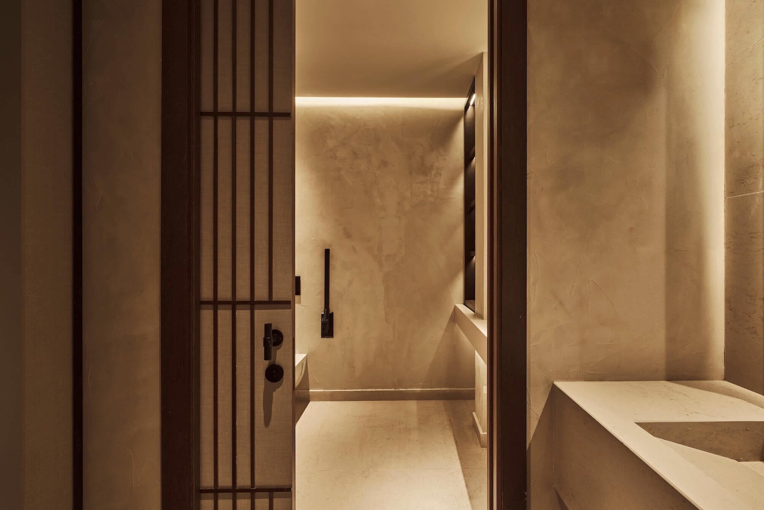 A modern bathroom with a minimalist design, featuring a large mirror, a sink, and a door with vertical bars.