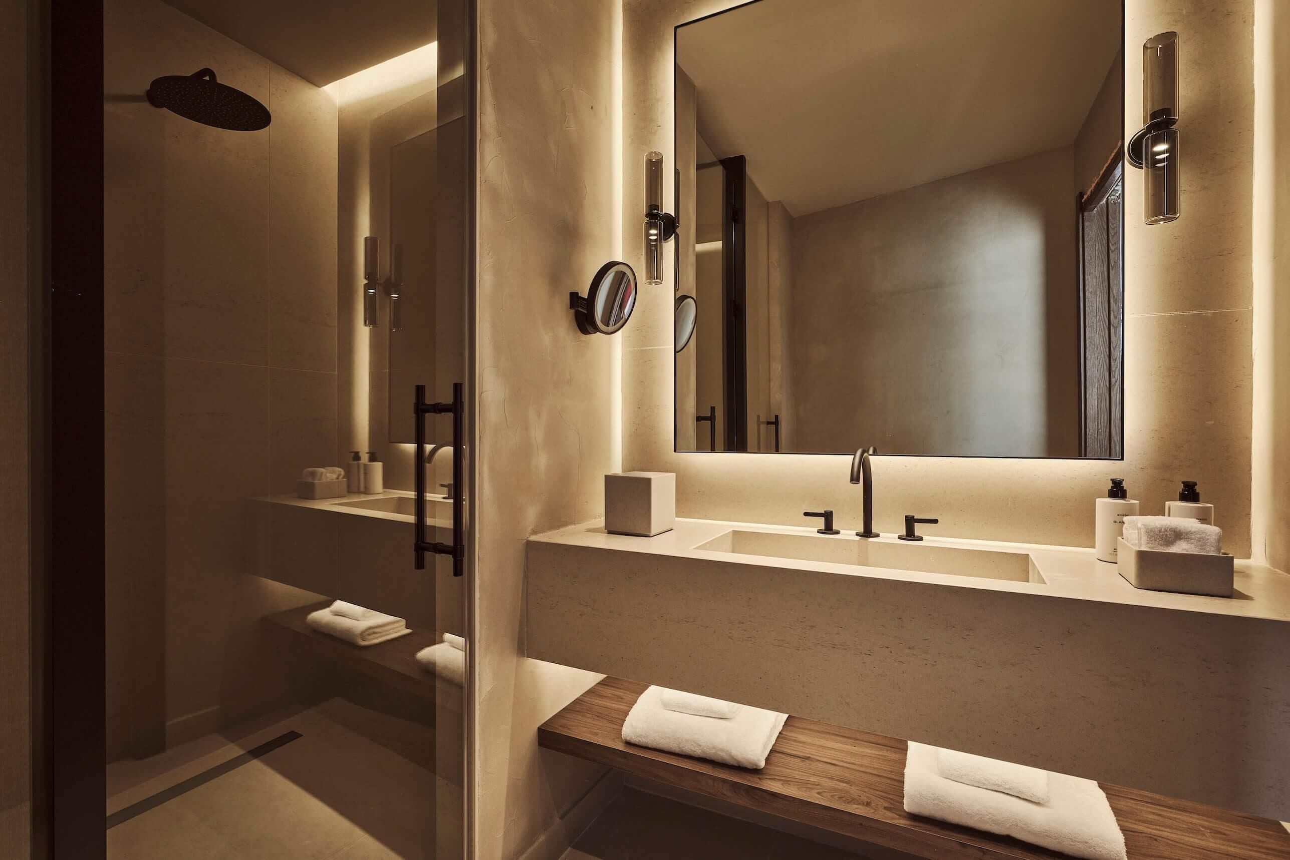 A modern bathroom with a large mirror, two sinks, a shower, and a wooden vanity.