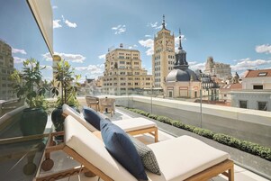 Terraço no telhado com espreguiçadeiras, plantas em vasos e vista para edifícios históricos.