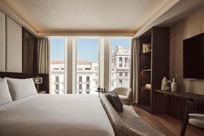 Une chambre d’hôtel avec un grand lit, un canapé, une télévision, une petite table avec une lampe et une vue sur la ville.