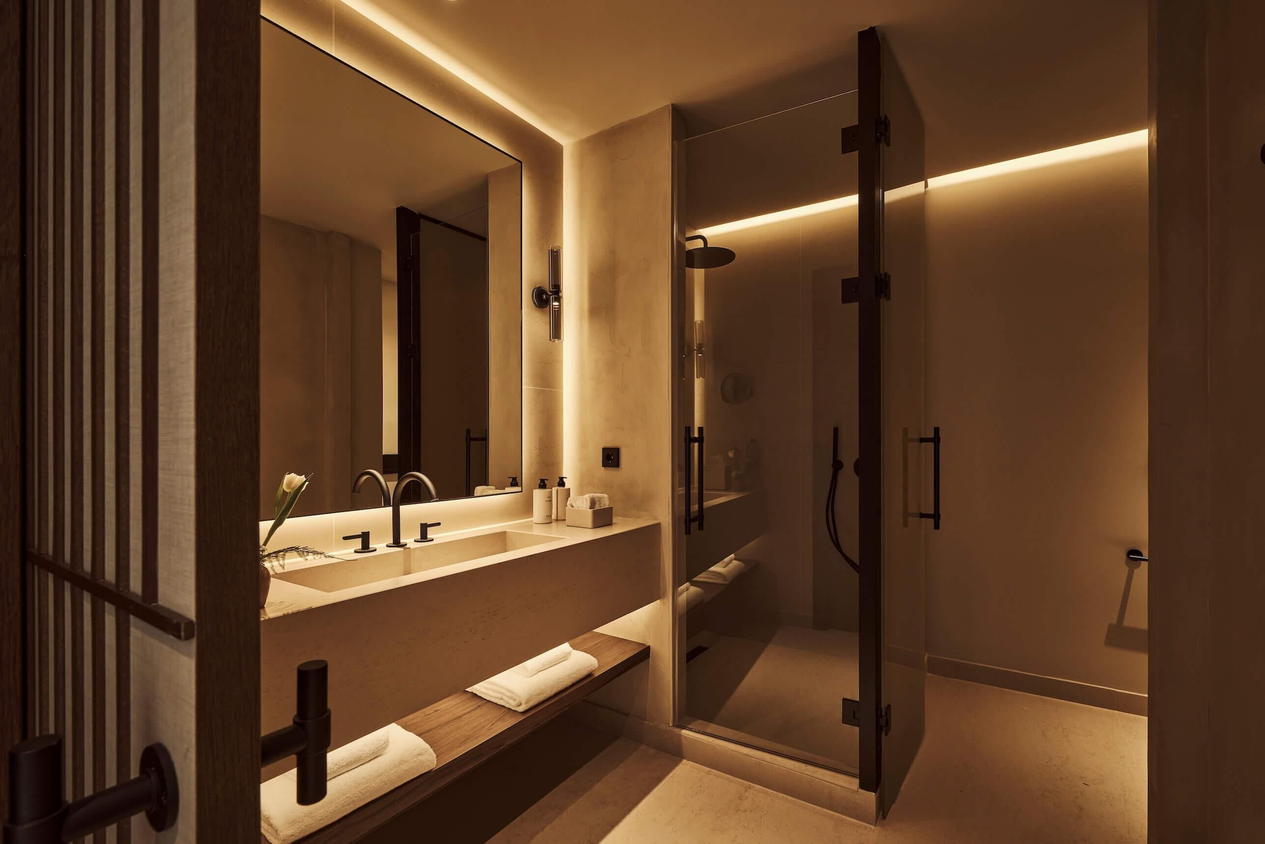 A modern bathroom with a large mirror, dual sinks, a shower enclosure, and a wooden vanity.