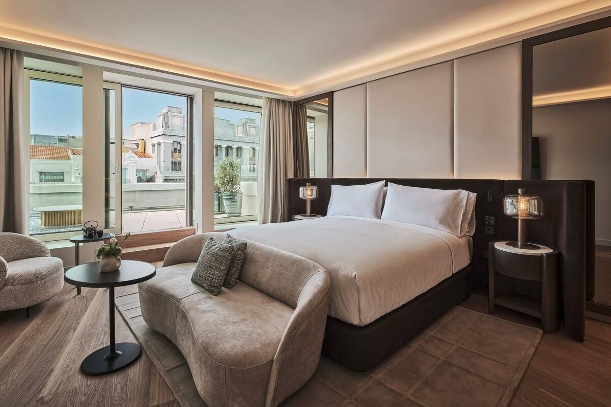 Moderni hotellihuone, jossa on suuri sänky, sohva, pieni pöytä ja näkymä kaupunkiin.