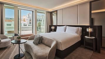 A modern hotel room with a large bed, a sofa, a small table, and a view of the city.