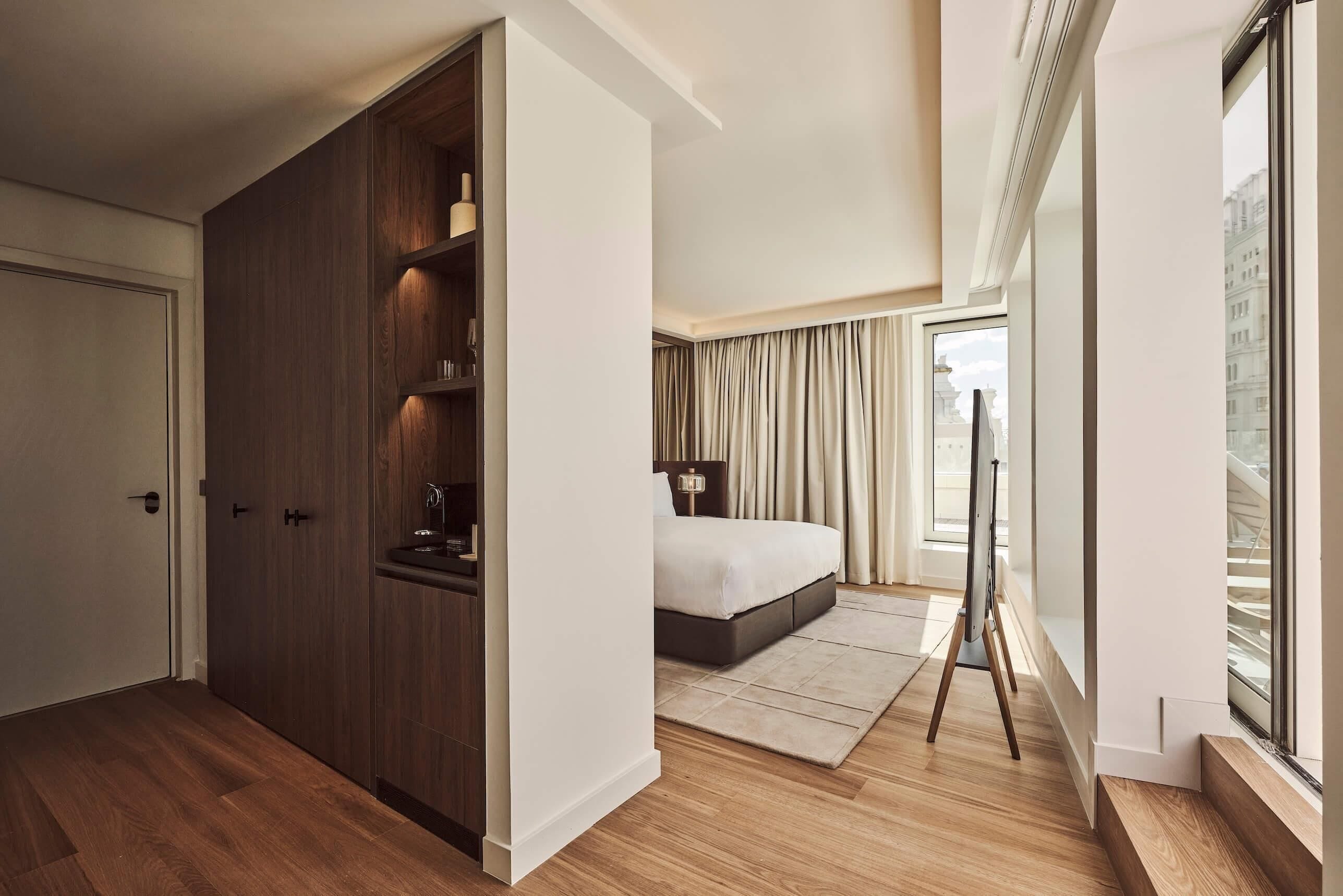 A bedroom with a bed, a wardrobe, a standing lamp, and a large window.