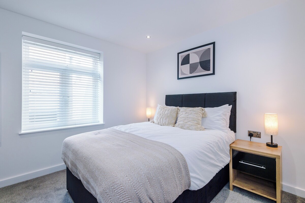 A bedroom with a bed, bedside tables, a wall-mounted artwork, and a window with blinds.