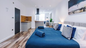 Moderni hotellihuone, jossa on suuri sänky, työpöytä, pieni keittiö ja näkymä kaupunkiin.