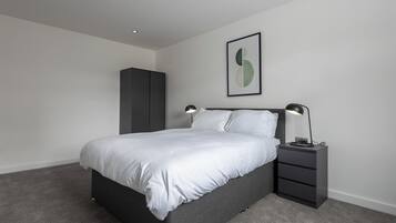 A modern bedroom with a bed, bedside tables, a wardrobe, and a framed artwork on the wall.