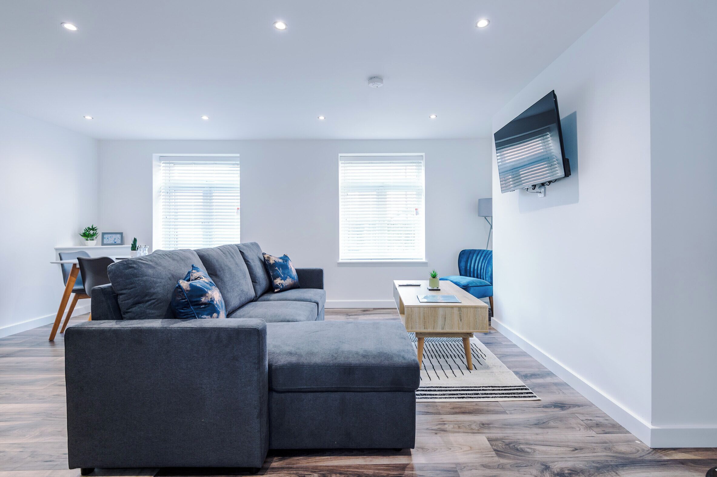 A modern living room with a sectional sofa, a coffee table, and a flat-screen TV mounted on the wall.