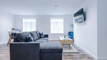 A modern living room with a sectional sofa, a coffee table, and a flat-screen TV mounted on the wall.