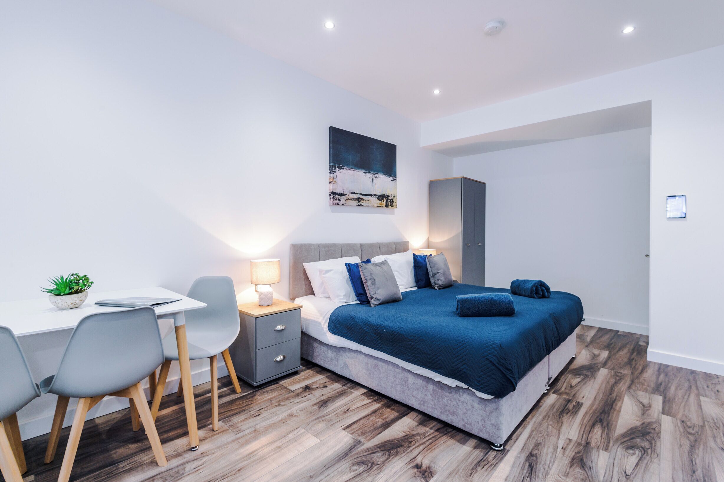 A modern bedroom with a bed, bedside table, lamp, and a desk with chairs.