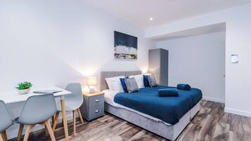 A modern bedroom with a bed, bedside table, lamp, and a desk with chairs.