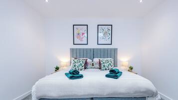 A neatly arranged bedroom with a bed, pillows, two wall-mounted lights, and two framed artworks.