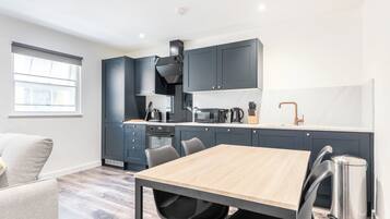 Une cuisine moderne avec des meubles de couleur sombre, une table à manger en bois et une poubelle en acier inoxydable.