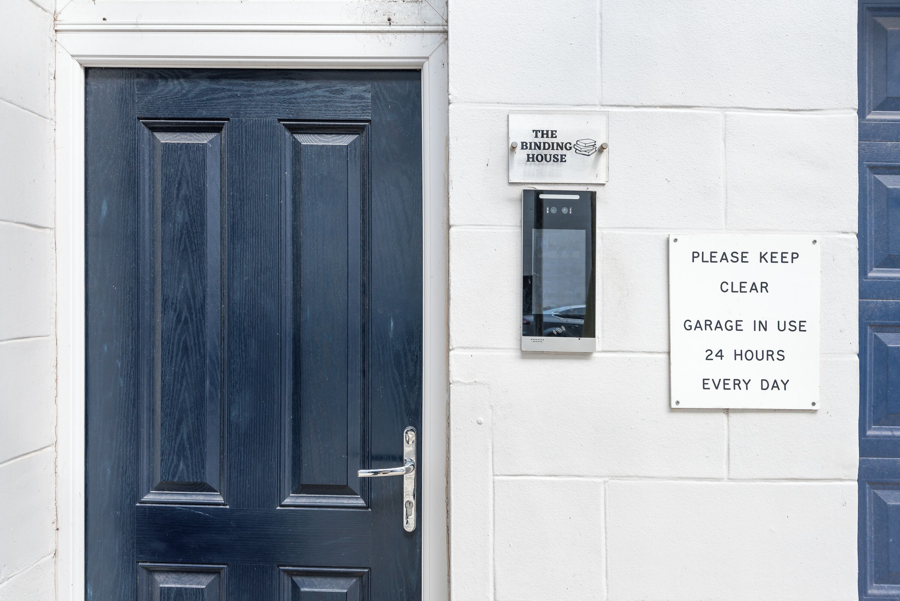A dark blue door with a metal handle and a sign stating 'PLEASE KEEP CLEAR GARAGE IN USE 24 HOURS EVERY DAY.'