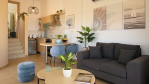 Una sala moderna con un sofá gris, una mesa de centro y un comedor con sillas, con una pequeña cocina al fondo.