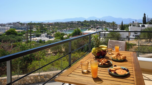 Un balcón con una mesa dispuesta para el desayuno y vista a un pueblo costero y montañas.