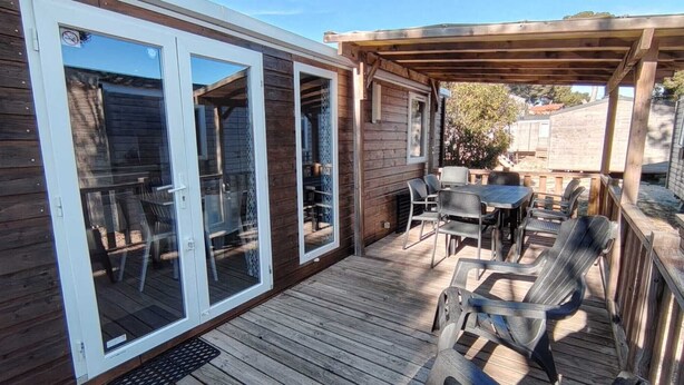 Una terraza de madera con pérgola, puertas de cristal correderas y mobiliario exterior.