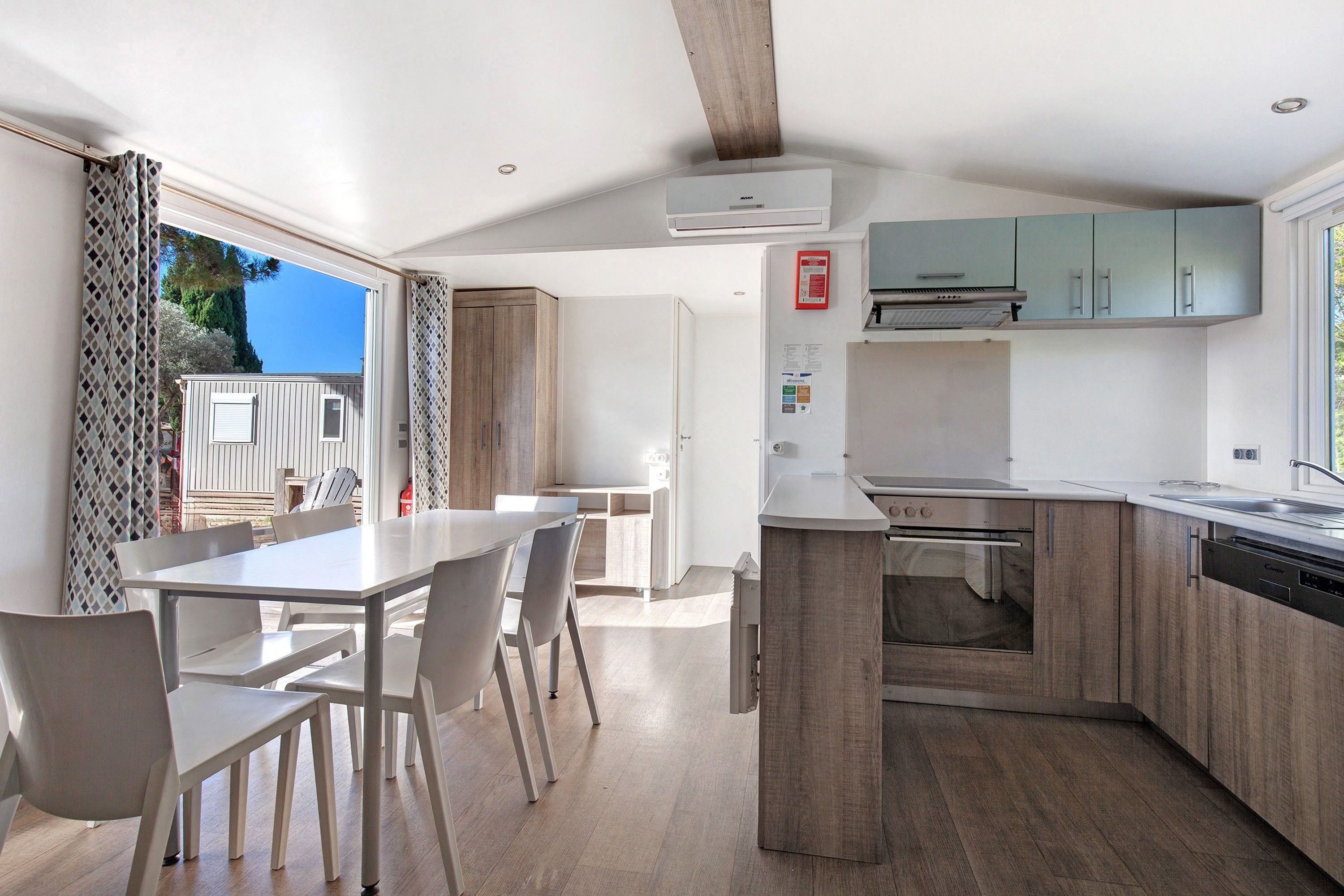 A modern kitchen with a built-in oven and dishwasher, wooden cabinets, and a dining area with a table and chairs.
