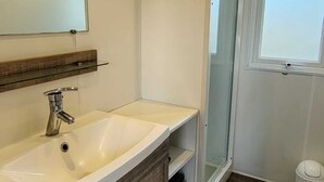 Un baño con lavamanos blanco, espejo, cabina de ducha y ventana.