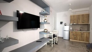 Una cocina moderna con armarios empotrados, un televisor de pantalla plana, una zona de comedor con una mesa y sillas blancas, y un banco gris.
