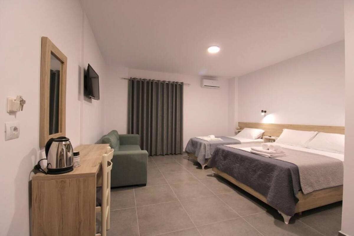 A hotel room with a bed, a desk with a kettle, a chair, a TV, and a curtain.