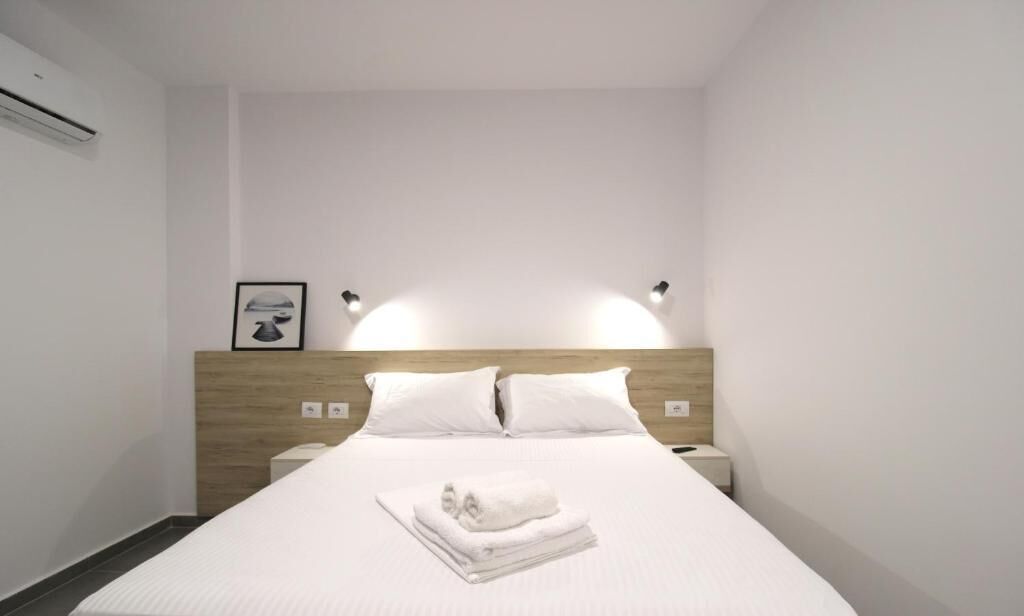 Une chambre d’hôtel avec un lit bien fait, deux tables de chevet, une tête de lit et des lampes fixées au mur.