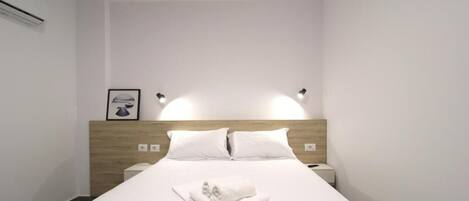 Une chambre d’hôtel avec un lit bien fait, deux tables de chevet, une tête de lit et des lampes fixées au mur.
