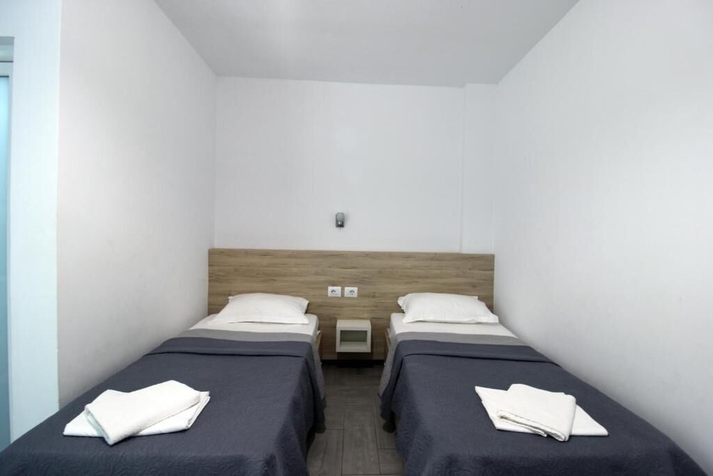Una habitación con dos camas, cabecero de madera, mesita de noche pequeña y lámpara de pared.