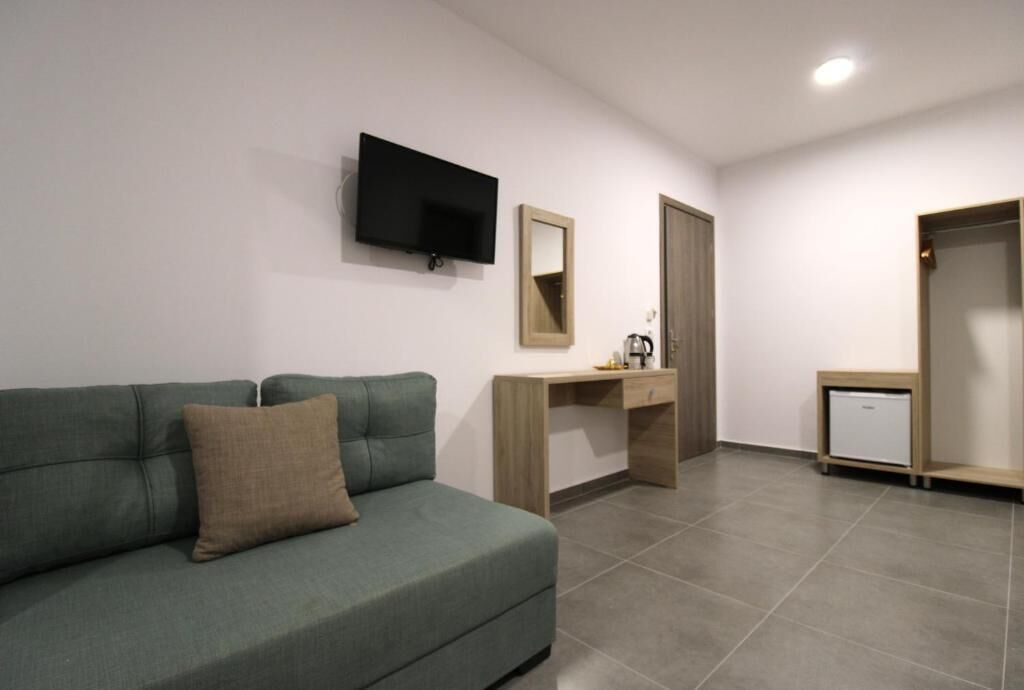 A room with a green sofa, a wooden desk, a television, a mirror, a wardrobe, and a small refrigerator.
